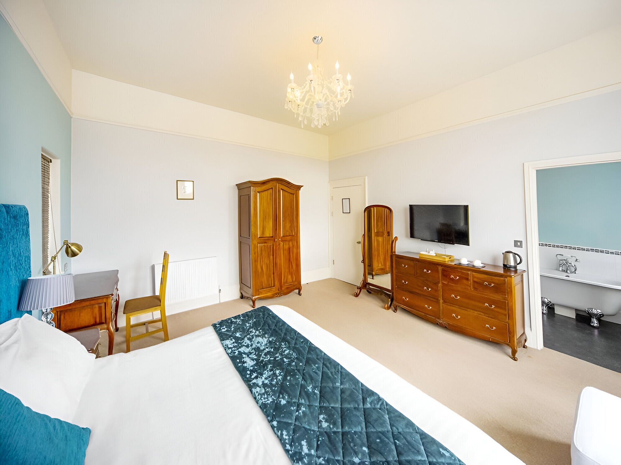 A bedroom with a bed, a dresser, a TV, and a bathroom visible through an open door.