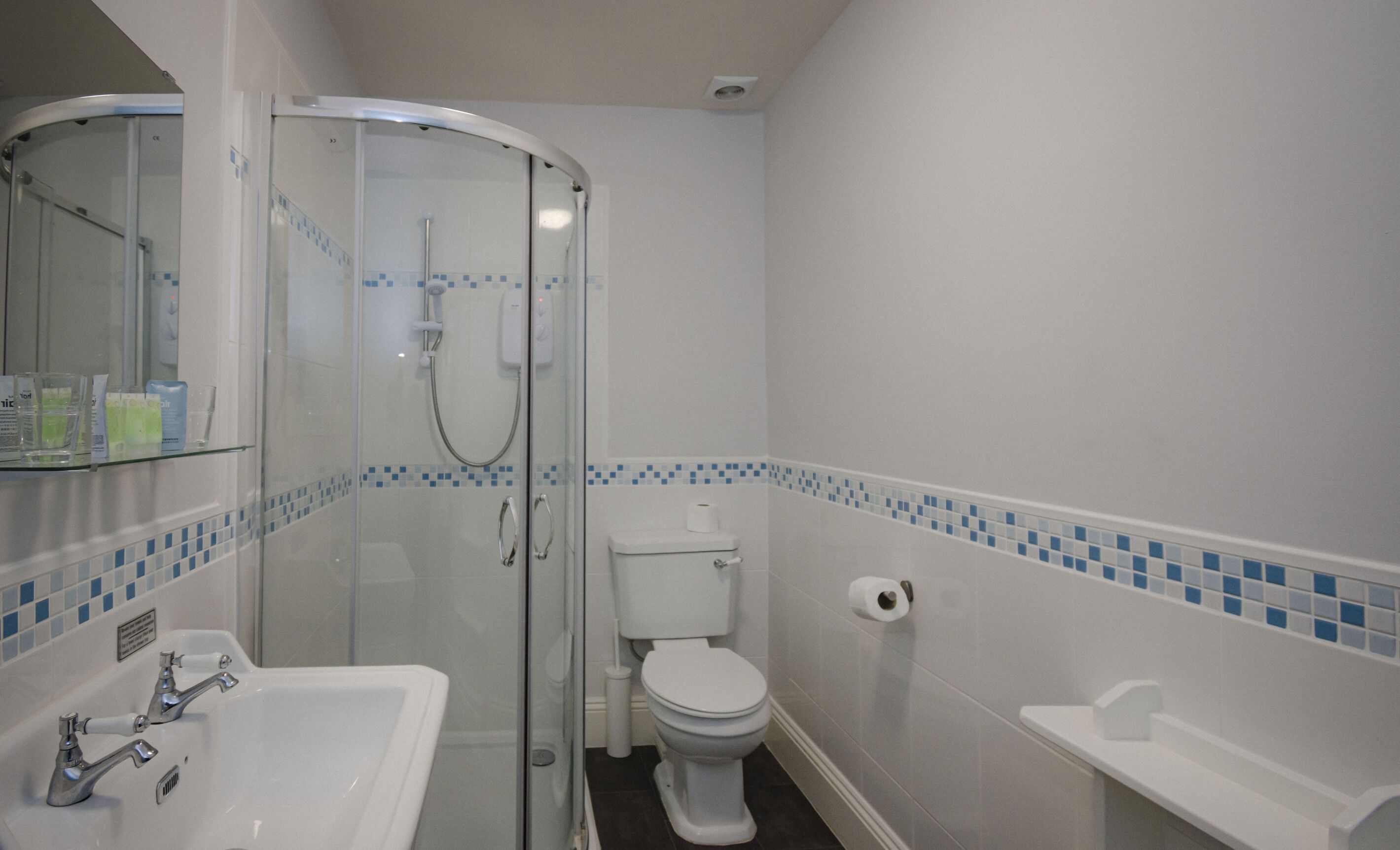 A bathroom with a glass-enclosed shower, a white toilet, and a white sink with two faucets.