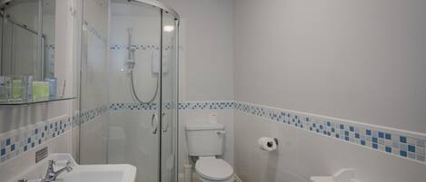 A bathroom with a glass-enclosed shower, a white toilet, and a white sink with two faucets.