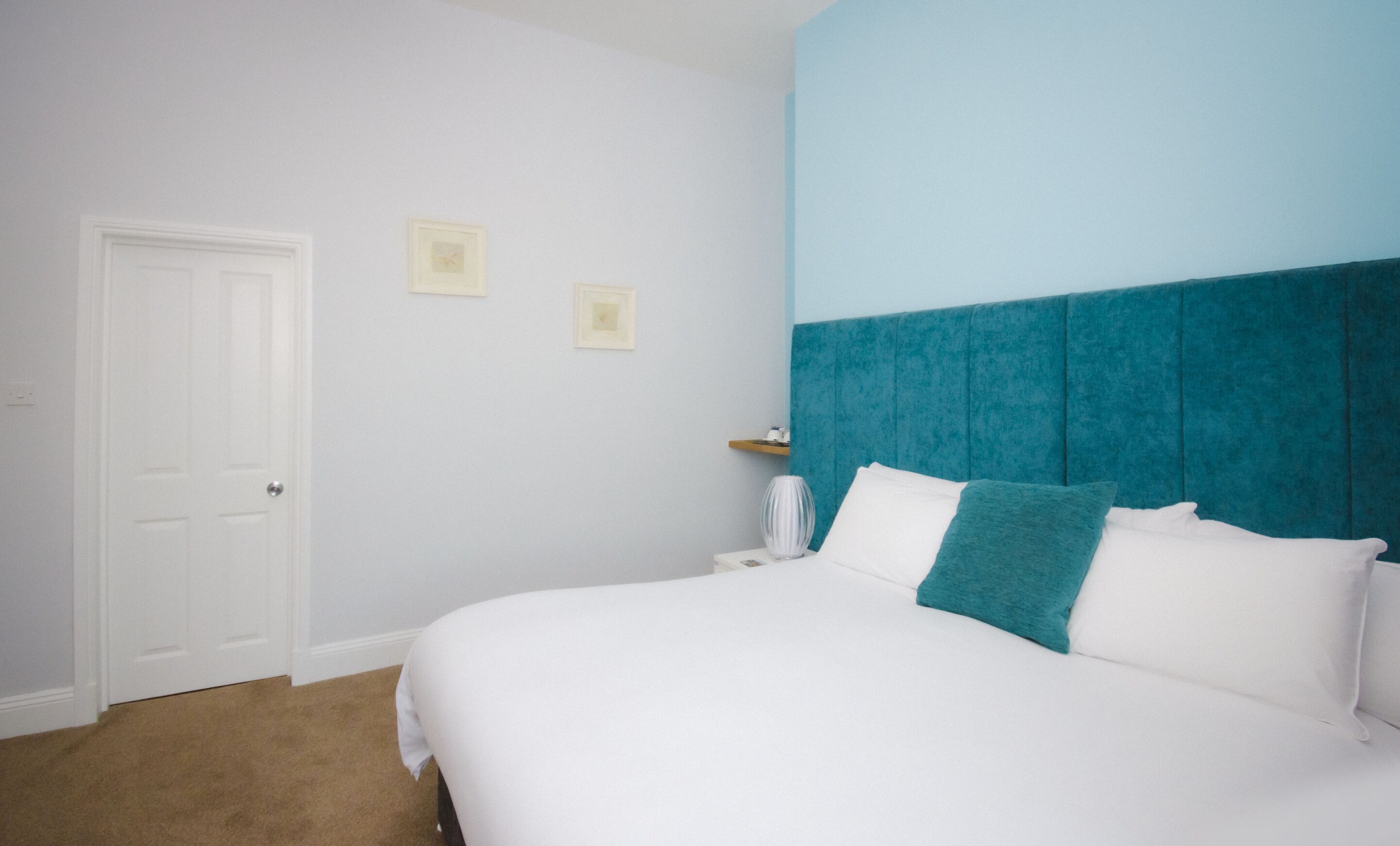 A bedroom with a white bed, teal headboard, and a white door.