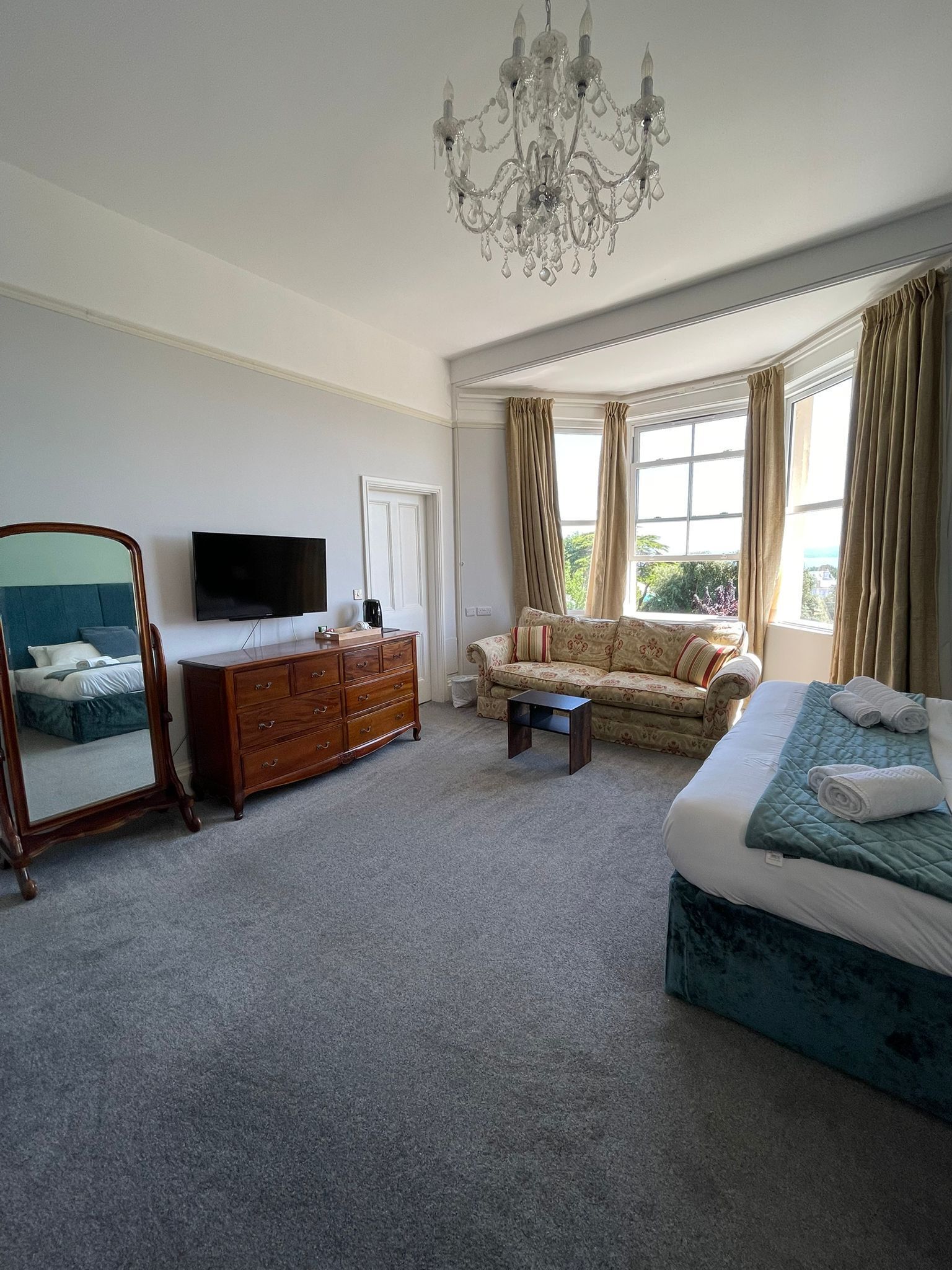 A spacious bedroom with a large bed, a sofa, a TV, a dresser, and a chandelier.
