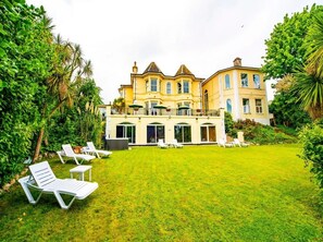 A large, two-story building with a spacious lawn and white lounge chairs. - Crofton House Hotel (Torquay)