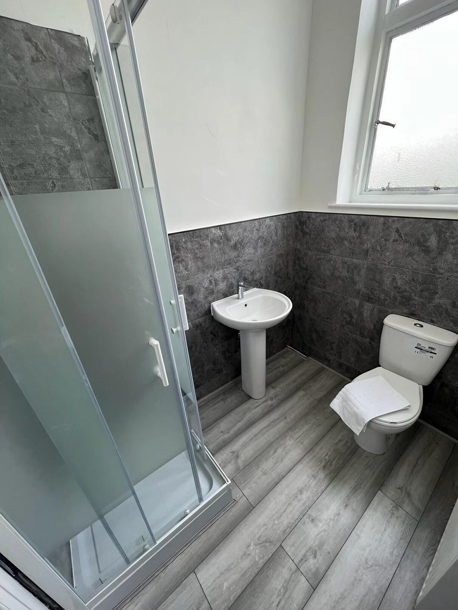 Baño con cabina de ducha de vidrio, lavamanos pedestal y retrete.