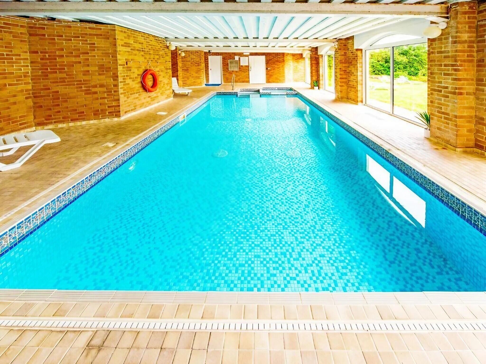 An indoor swimming pool with clear blue water, surrounded by brick walls and a tiled floor.