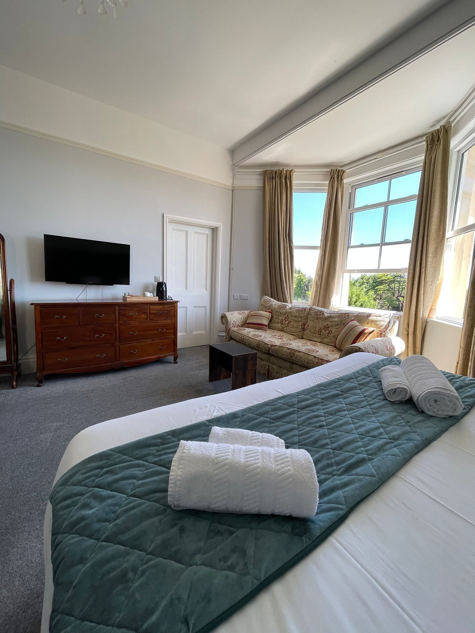 A hotel room with a bed, a dresser, a television, and a window with curtains.
