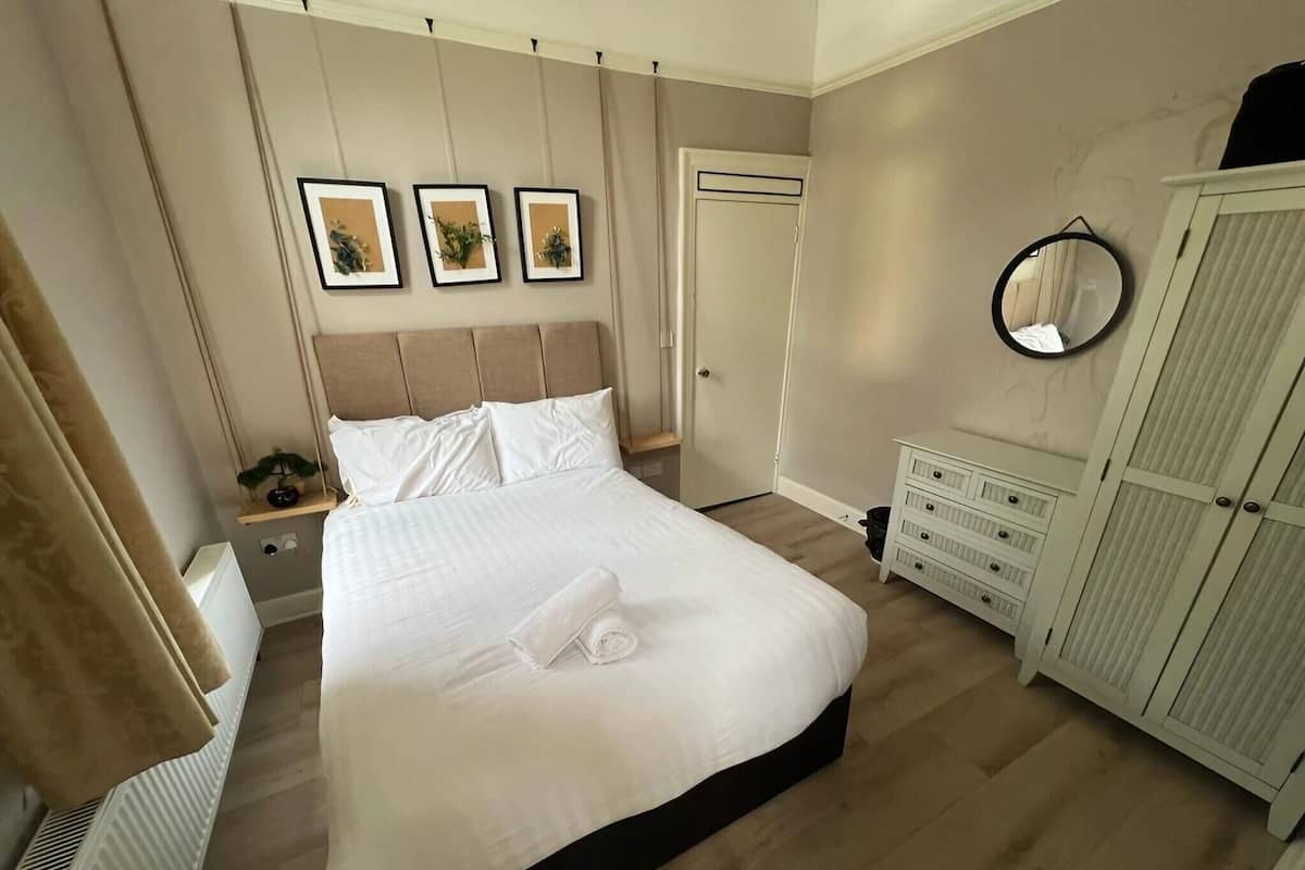 A neatly arranged bedroom with a large bed, a dresser, a wardrobe, and three framed pictures on the wall.