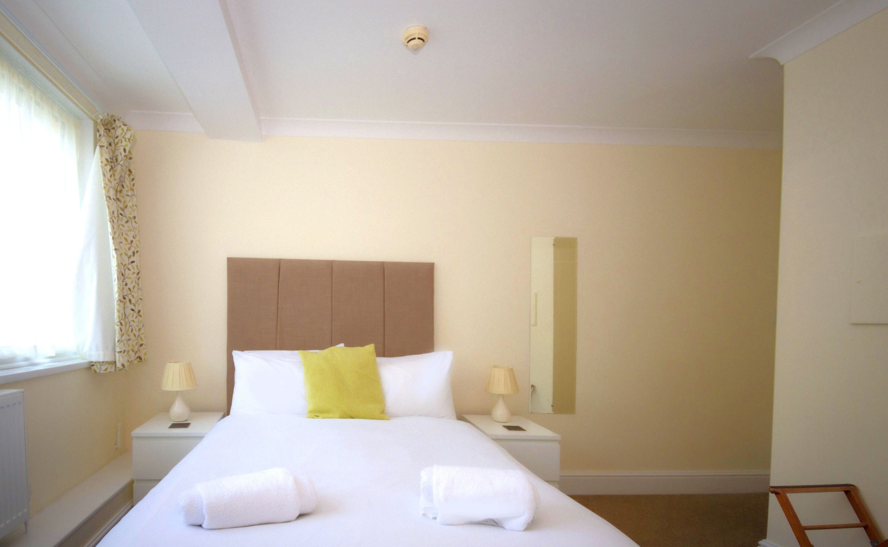 A hotel room with a large bed, two bedside tables with lamps, a headboard, and a window with curtains.