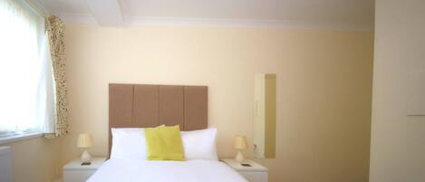 A hotel room with a large bed, two bedside tables with lamps, a headboard, and a window with curtains.