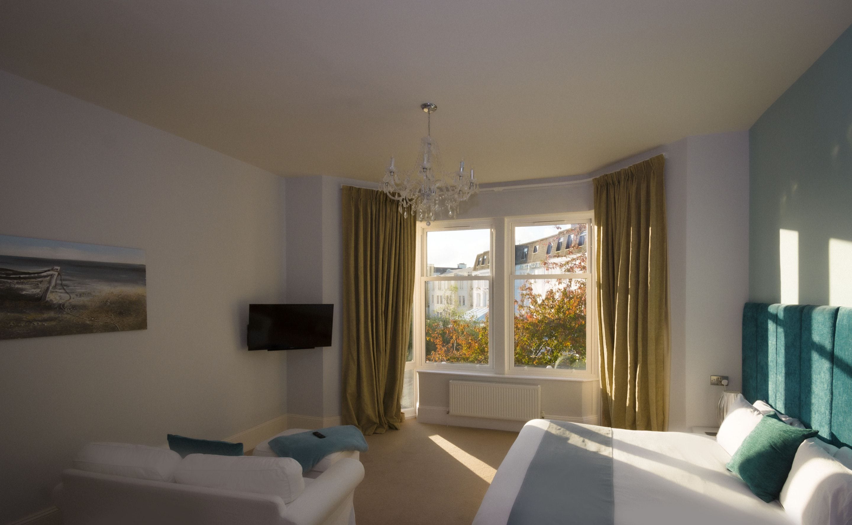 A hotel room with a bed, a sofa, a TV, and a window with curtains.