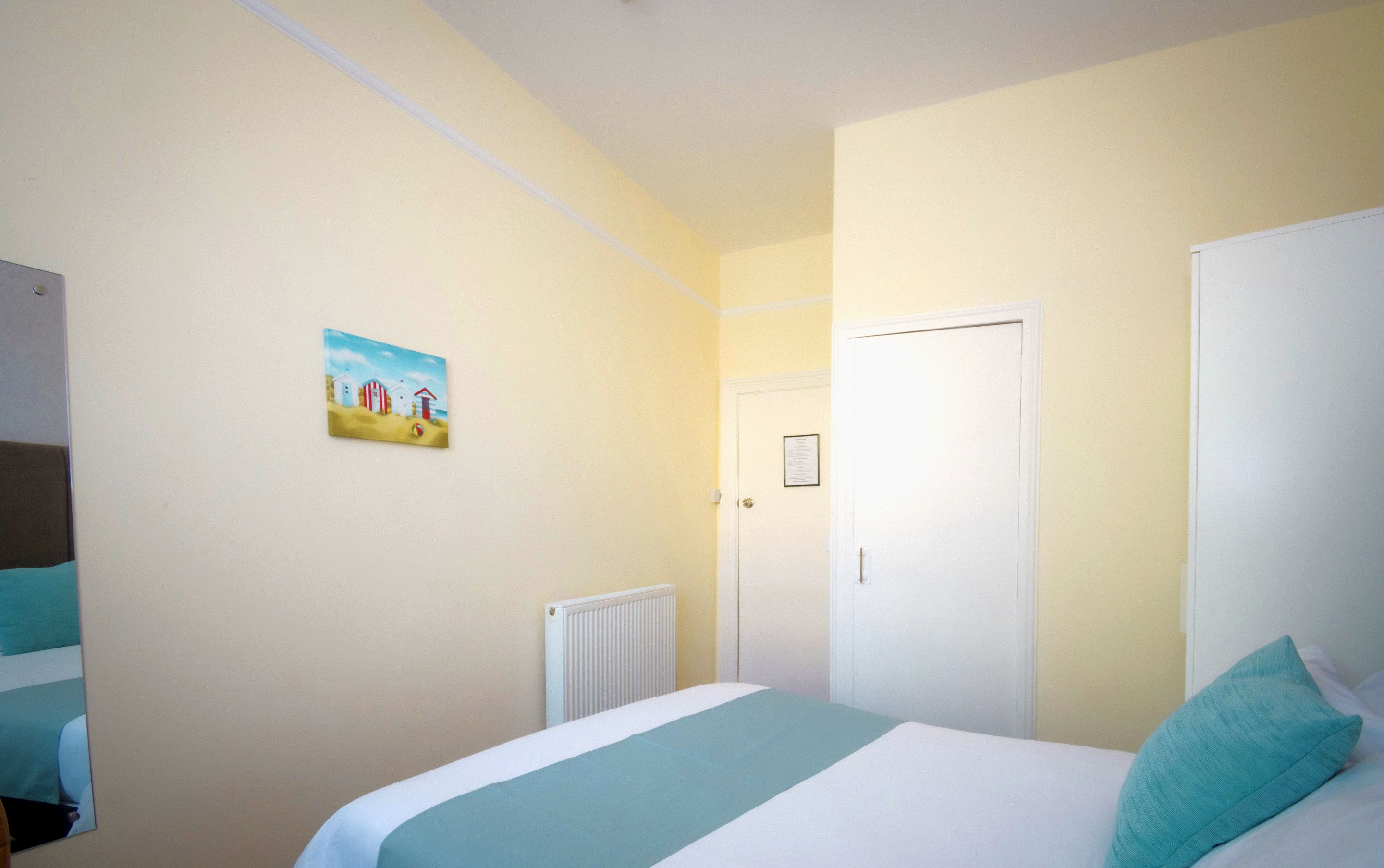 A bedroom with a bed, a radiator, a door, and a painting on the wall.