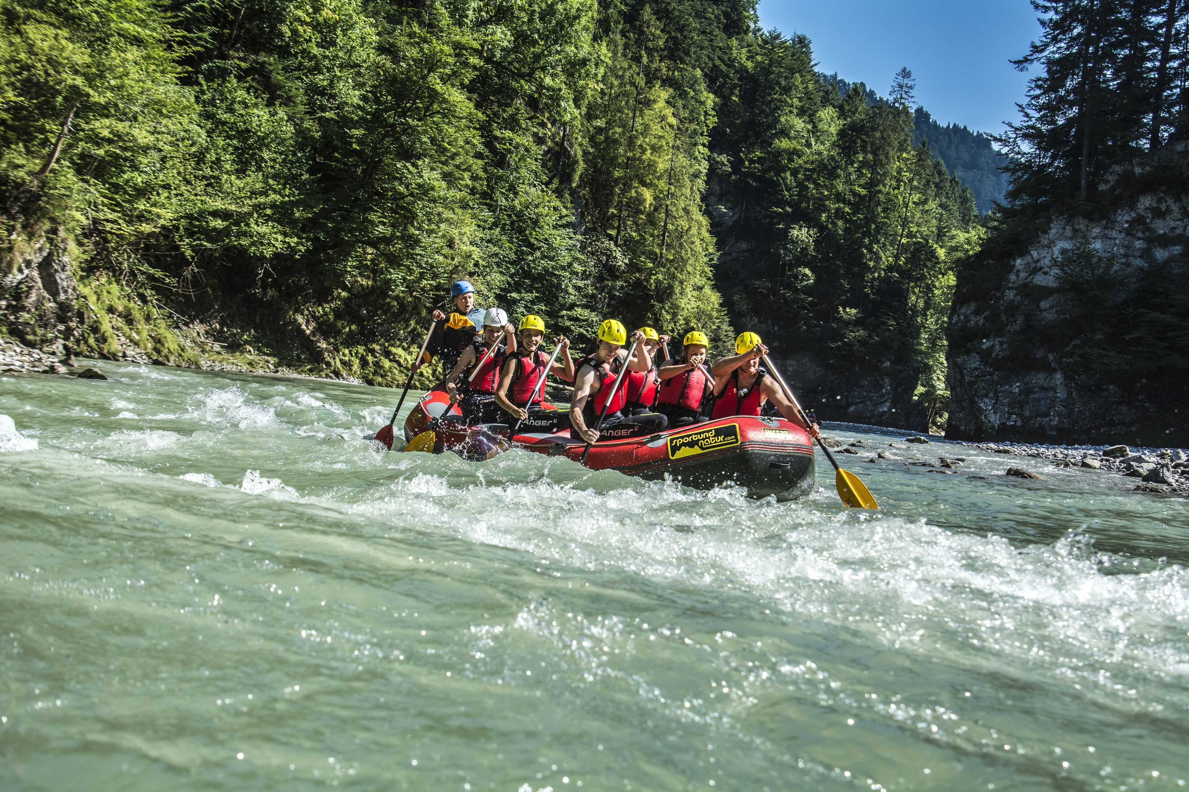 A group of people in a raft navigating a river surrounded by dense forest.