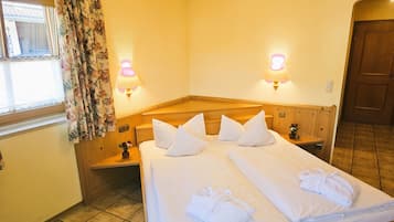 A hotel room with a large bed, two bedside tables, a wooden headboard, a window with floral curtains, and two wall-mounted lamps.