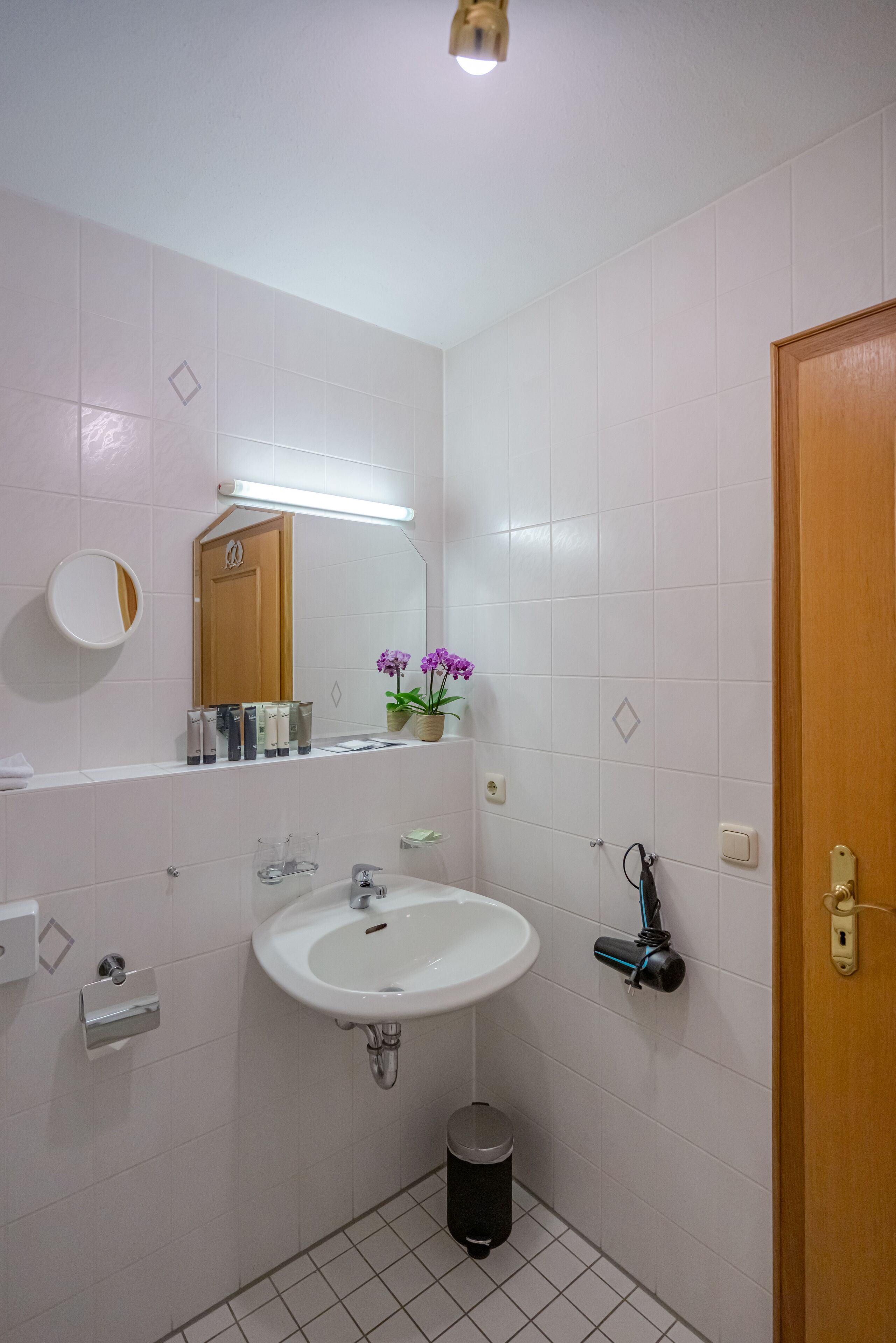Une salle de bain avec un lavabo blanc, un miroir et une porte en bois.