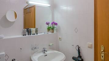Une salle de bain avec un lavabo blanc, un miroir et une porte en bois.