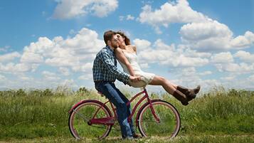 A couple on a bicycle in a grassy field with a clear sky.
