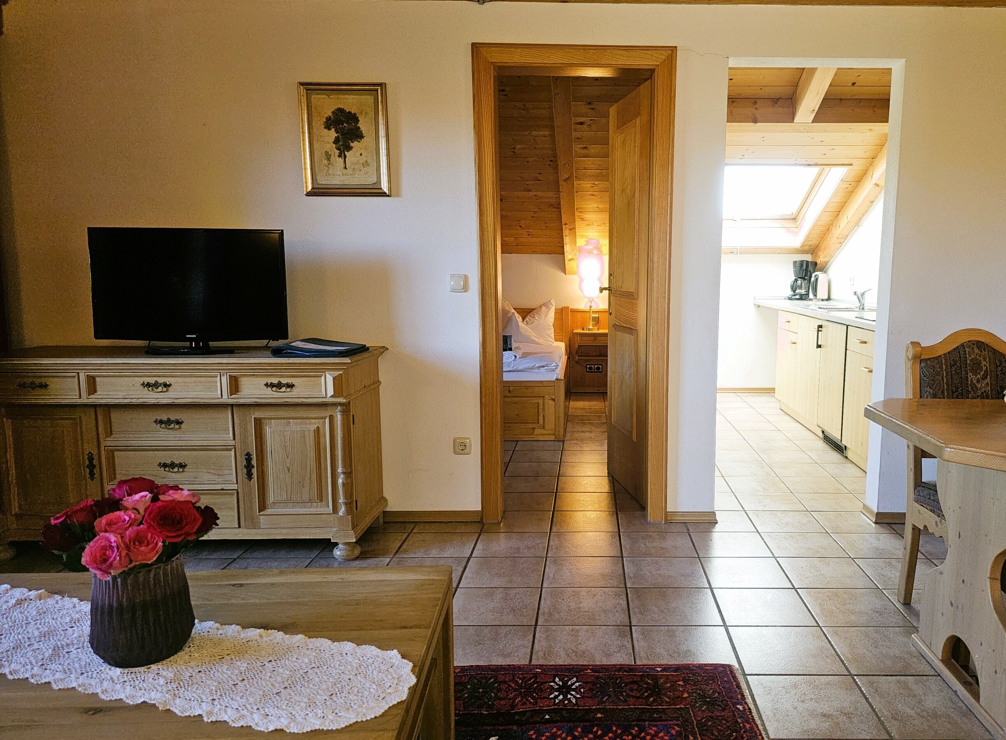 Una habitació acollidora amb televisió, un armari de fusta i un ram de flors.