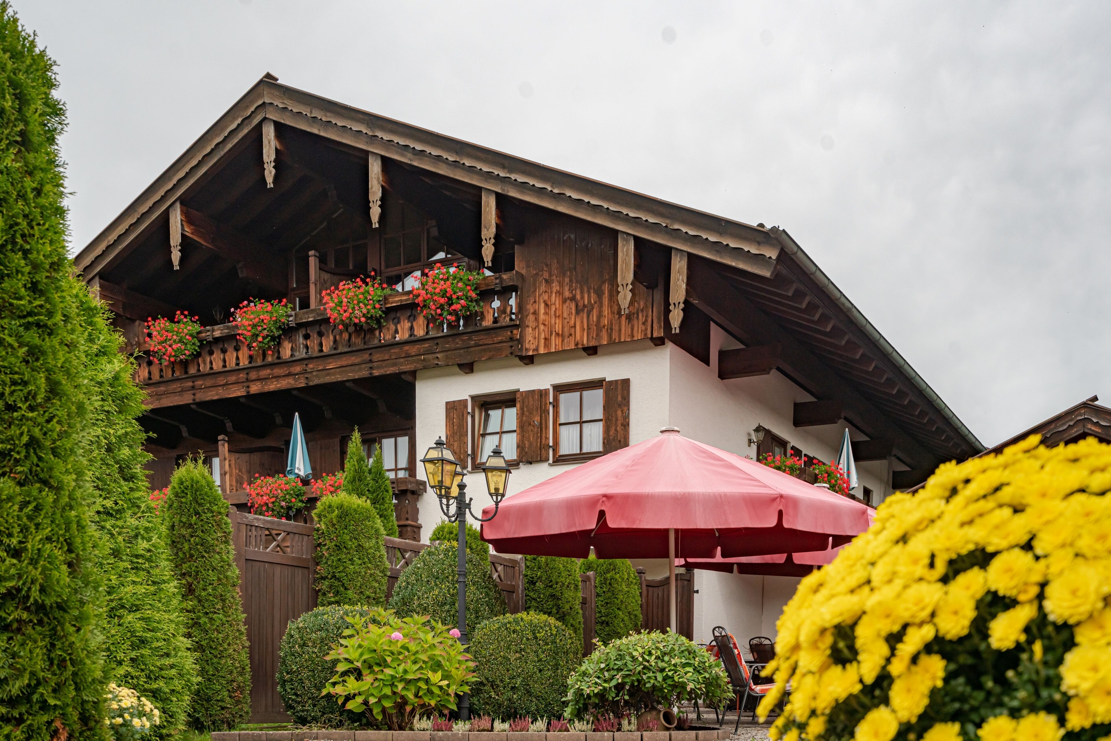Una chaleta tradicional con balcones de madera, un jardín con diversas plantas y mobiliario exterior con sombrillas.