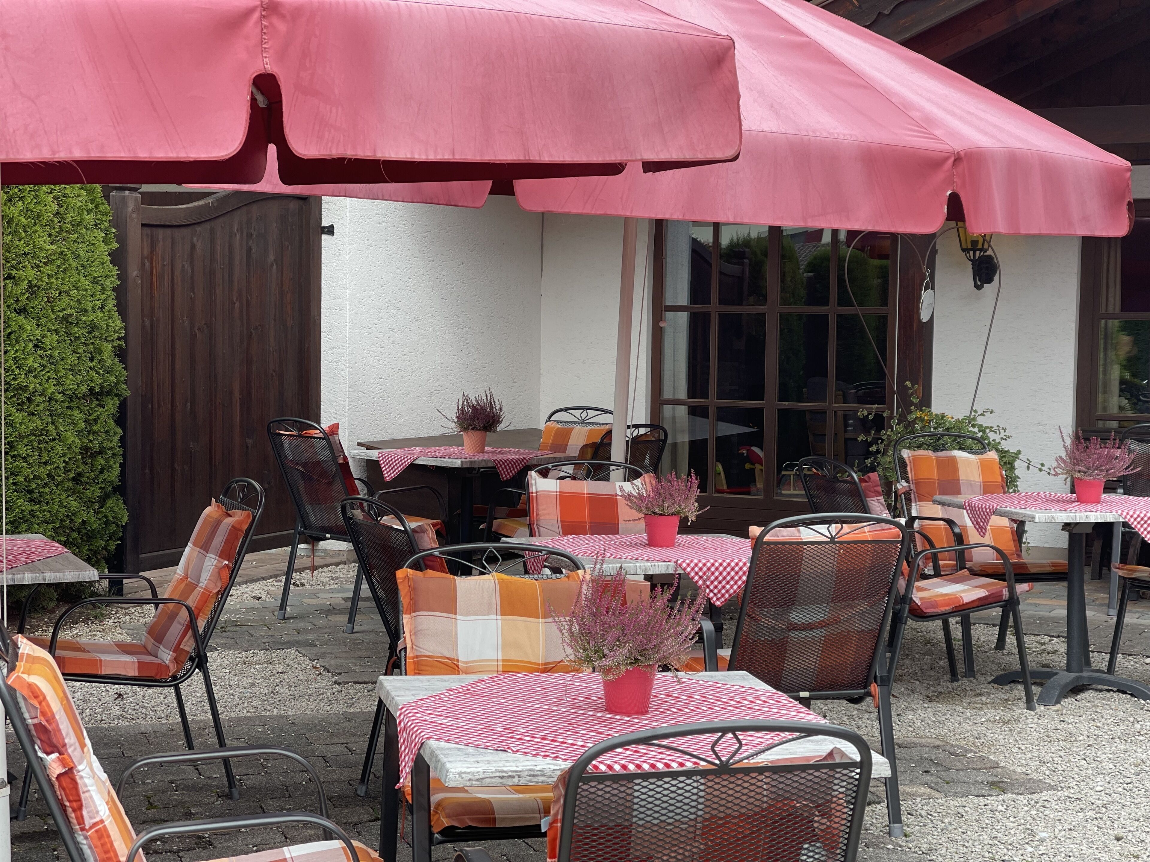 An outdoor patio with tables and chairs, covered by pink umbrellas, and a wooden fence in the background.