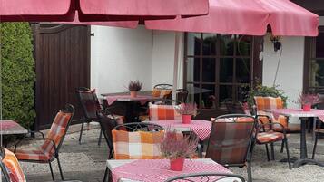 An outdoor patio with tables and chairs, covered by pink umbrellas, and a wooden fence in the background.