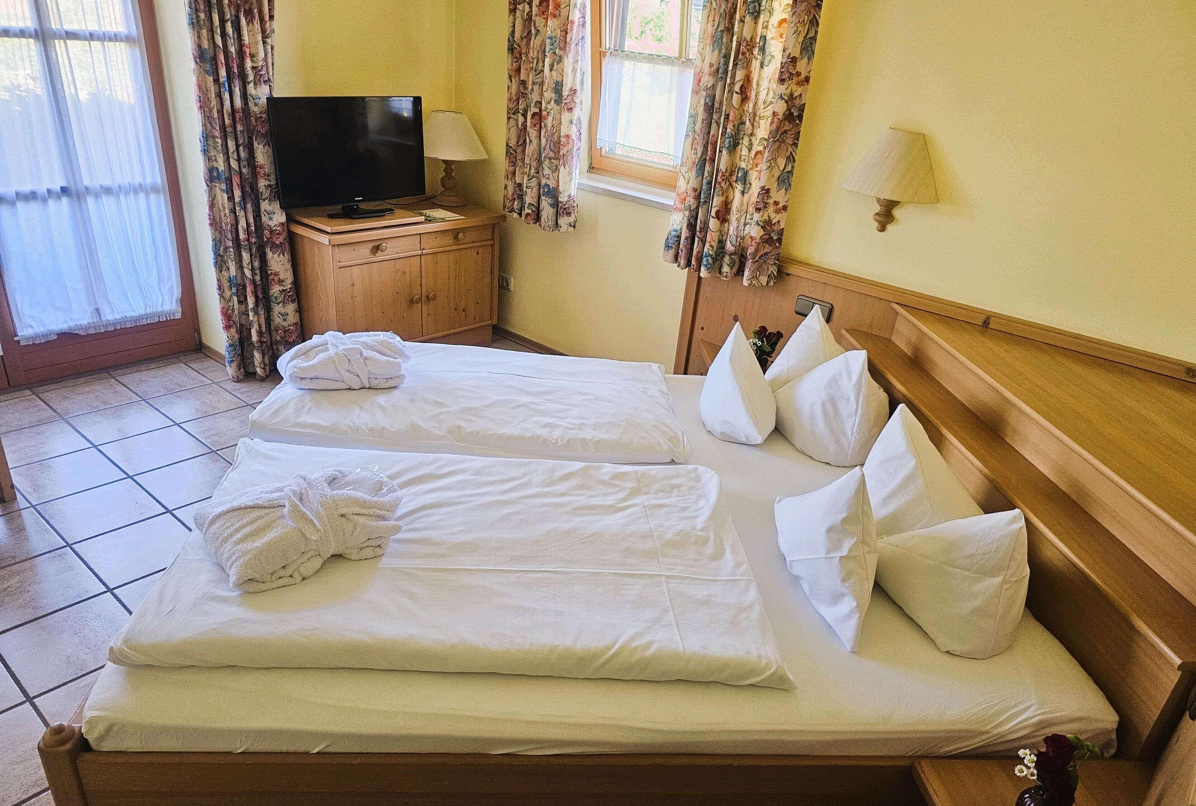 Habitación de hotel con dos camas, un televisor sobre un mueble de madera y cortinas estampadas.