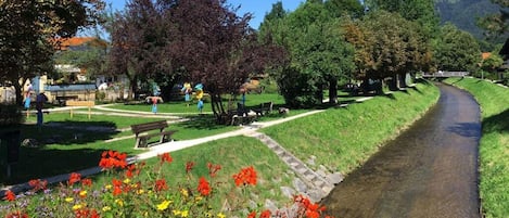Un parc avec un sentier dallé, des bancs et un petit ruisseau.