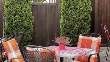 Une terrasse avec des chaises et une table en métal, protégée par un parasol rouge.