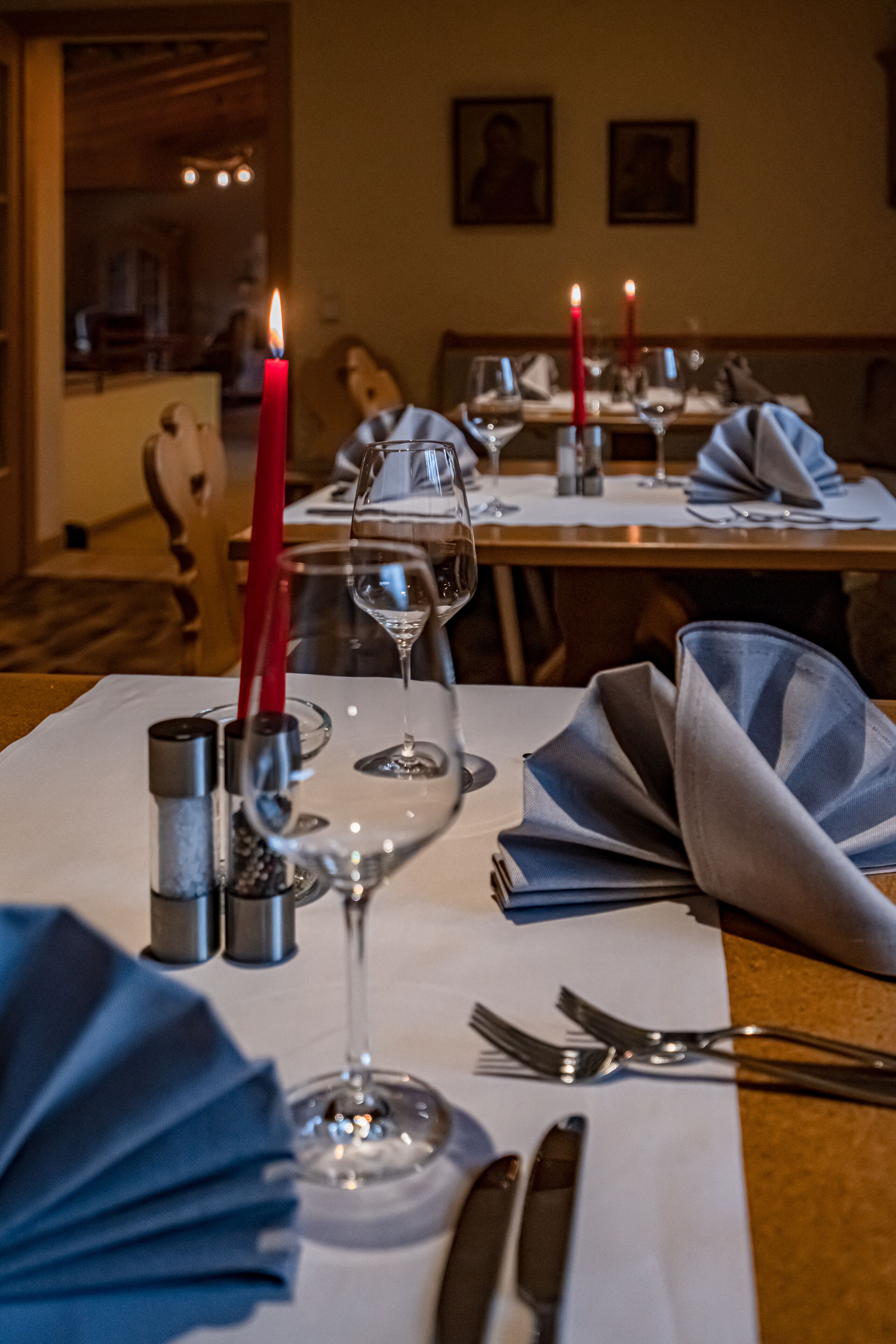 A dining table set with wine glasses, a red candle, salt and pepper shakers, and folded napkins.