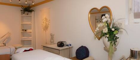 A bedroom with a bed, bedside table, lamp, and a heart-shaped mirror.