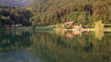Un lago tranquillo circondato da colline boscose, con il logo dell'hotel 'Achentaler Vital Hotel' nell'angolo in alto a sinistra.