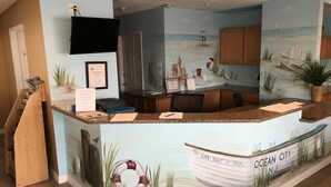 A reception desk with a mural of a beach scene, including a lifebuoy and a boat labeled "LIFE BOAT No 3420". - The Crossings (Ocean City)