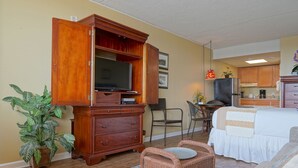 A hotel room with a wooden cabinet, a television, a bed, a dining area, and a kitchen. - The Crossings (Ocean City)