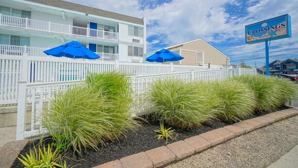 A beachfront hotel with a white fence, blue umbrellas, and a sign for 'Crossings Condominiums Rentals'. - The Crossings (Ocean City)