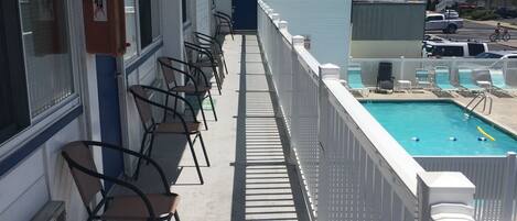 Un balcón de hotel con piscina, sillas y vista a la calle.