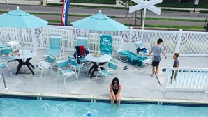 A swimming pool with lounge chairs and umbrellas, a white fence, and a flag. - The Crossings (Ocean City)