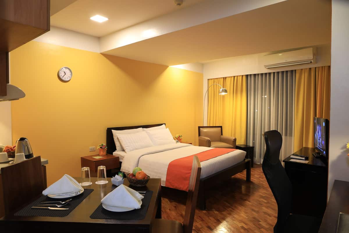 Una habitación de hotel con cama, escritorio, silla, televisor, reloj y aire acondicionado.