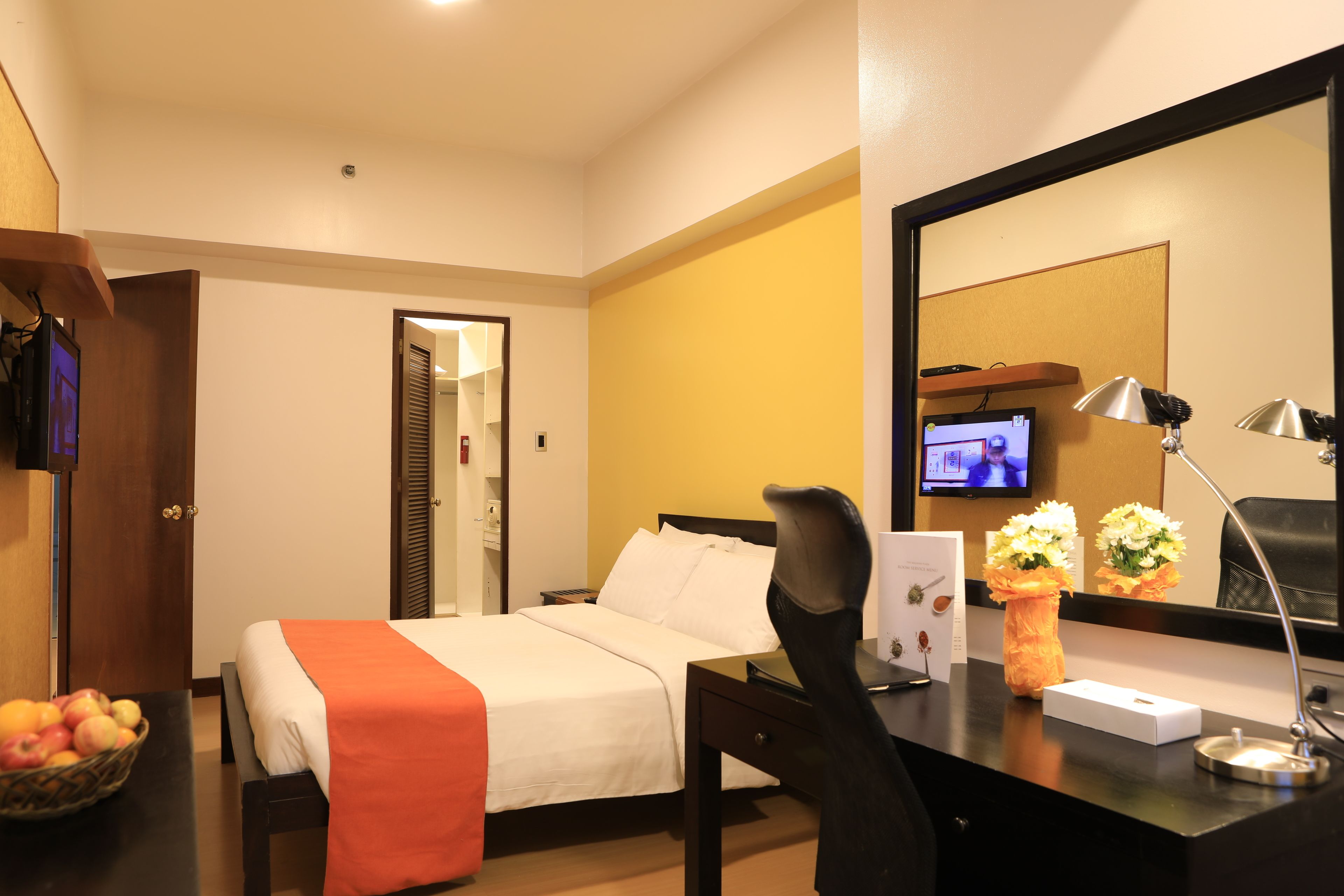 A hotel room with a bed, desk, chair, and a television on the wall.