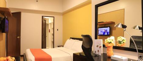 A hotel room with a bed, desk, chair, and a television on the wall.