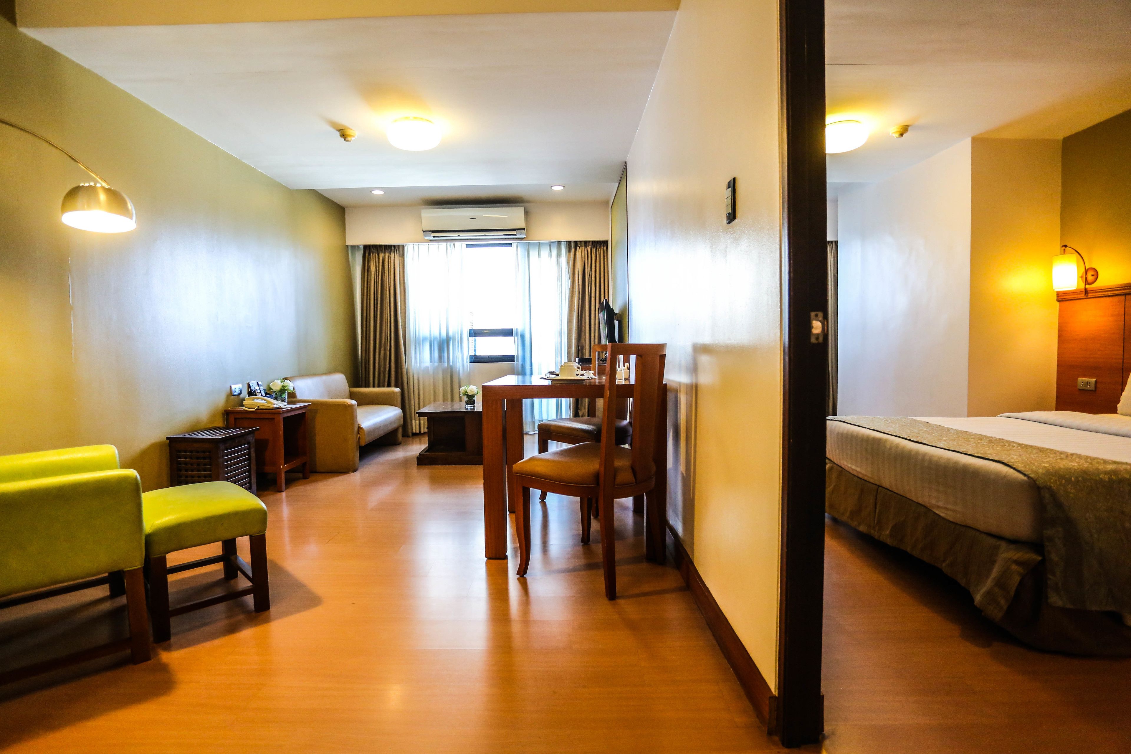 A hotel room with a bed, a dining table with chairs, a sofa, and a small table with a lamp.