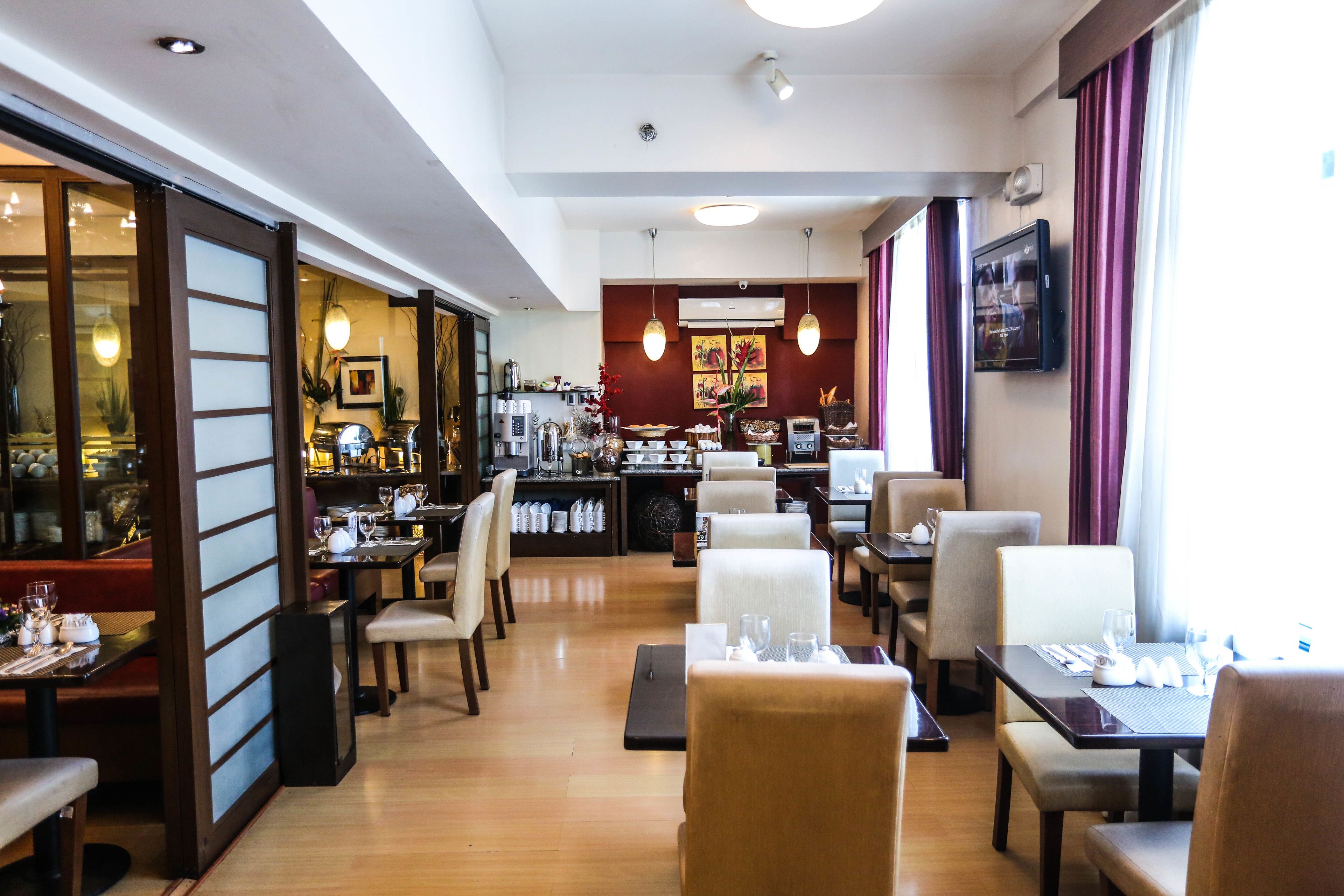 Zona de dinar d'un hotel amb diverses taules i caires, una barra al fons i vista al restaurant proper.