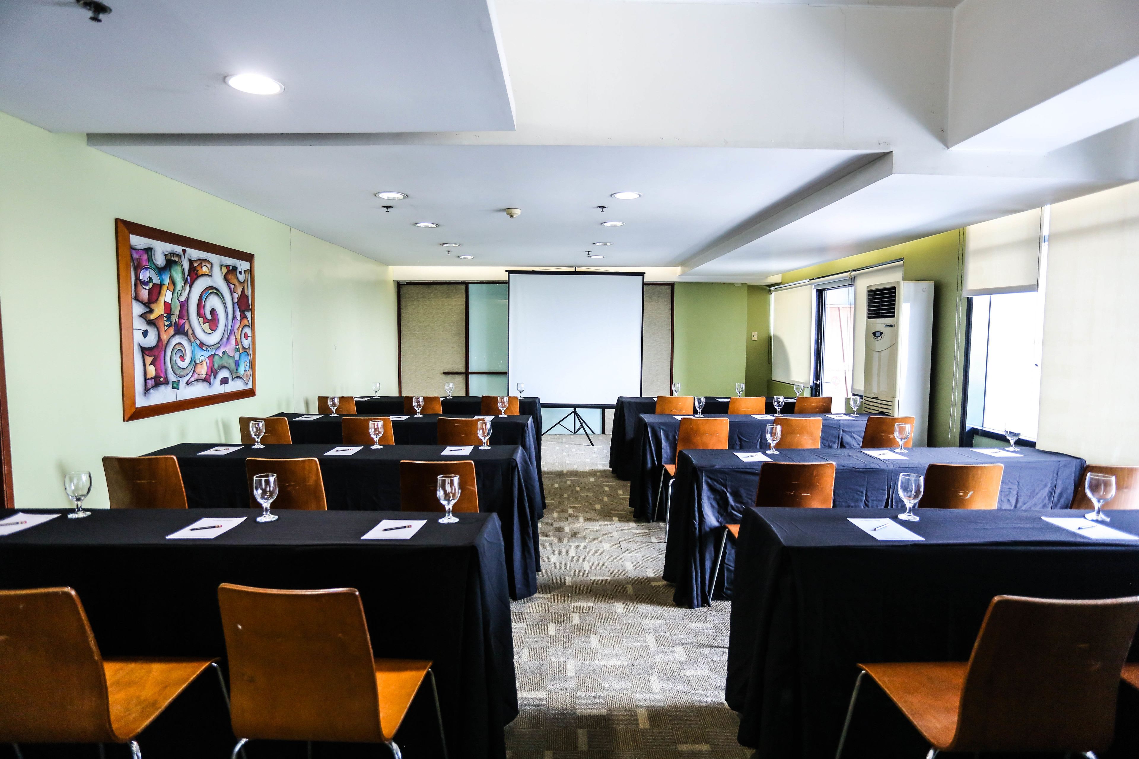 A conference room with tables set for a meeting, equipped with chairs and wine glasses.