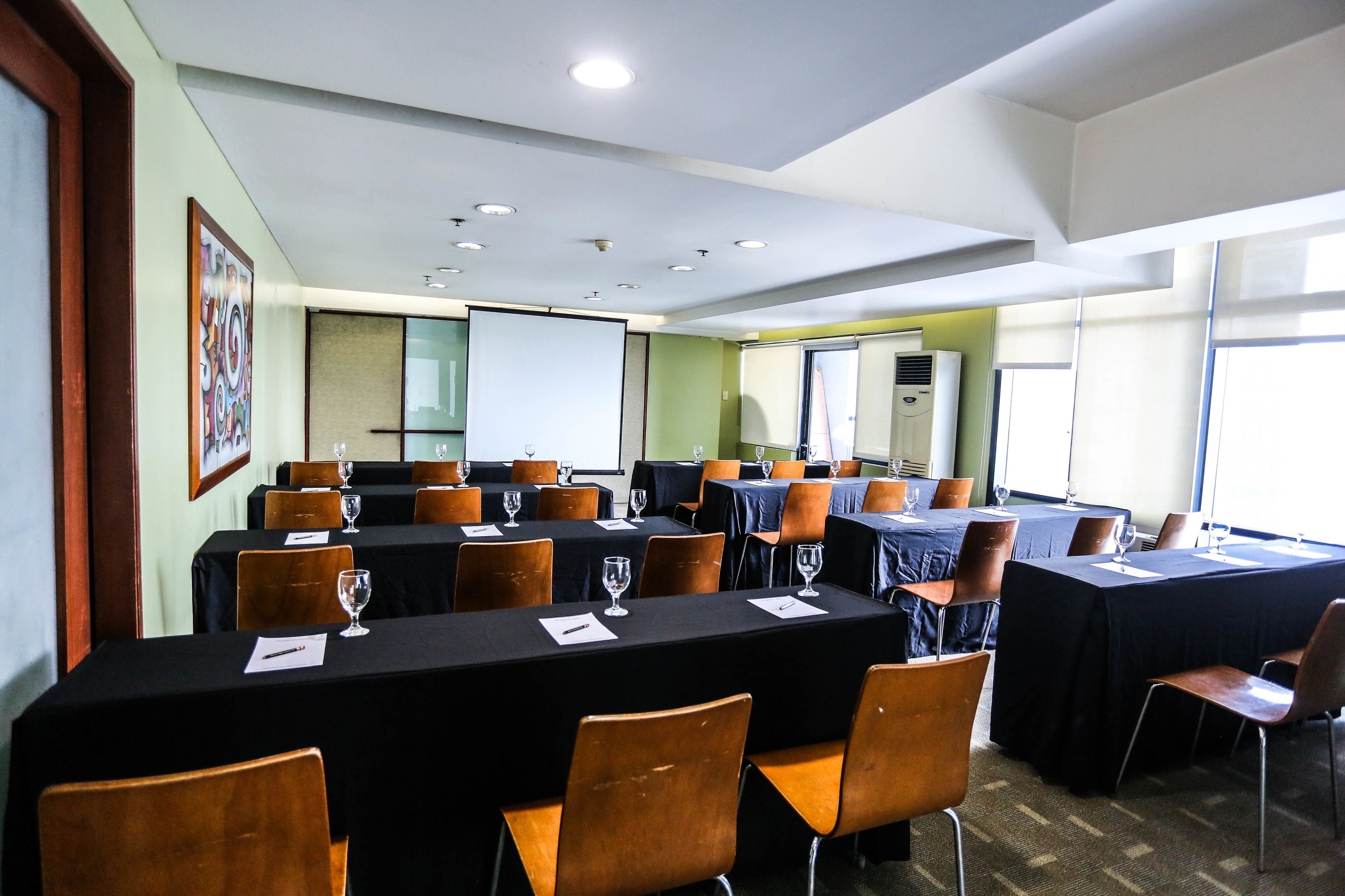 A conference room with multiple tables and chairs, equipped with glassware and papers, and large windows allowing natural light.