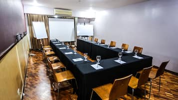 A conference room with a long table, chairs, a whiteboard, and a projector screen.