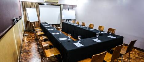 Una sala de conferencias con una larga mesa, sillas, una pizarra y una pantalla para proyector.