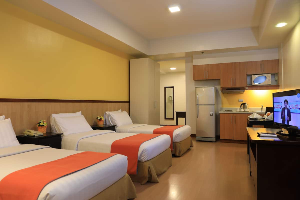 Habitación de hotel con tres camas, una kitchenette y un televisor.