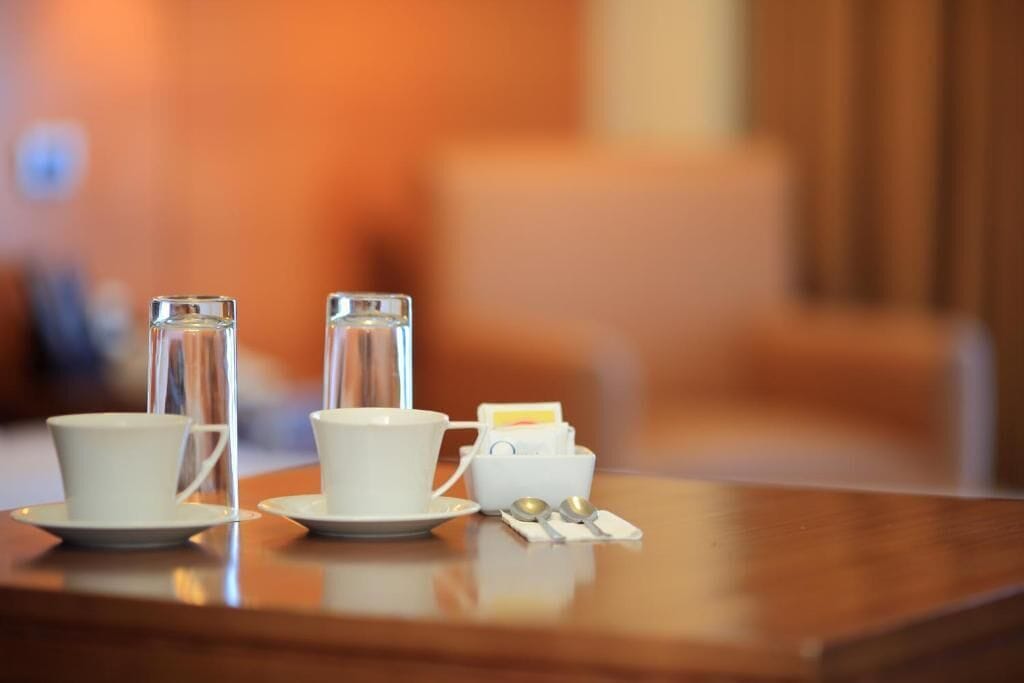 A table with two white cups and a small container, likely for tea or coffee, in a warmly lit room.