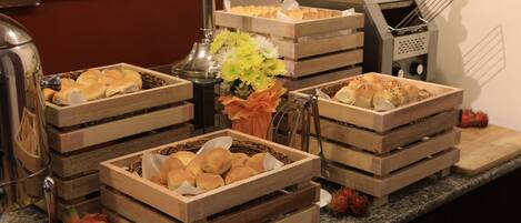 A buffet setup with various food items in wooden crates, a fruit bowl with dragon fruit and apples, and a decorative vase with flowers.