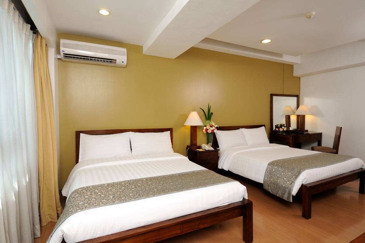 Habitación de hotel con dos camas, una mesita de noche con lámpara, un espejo y un equipo de aire acondicionado en la pared.