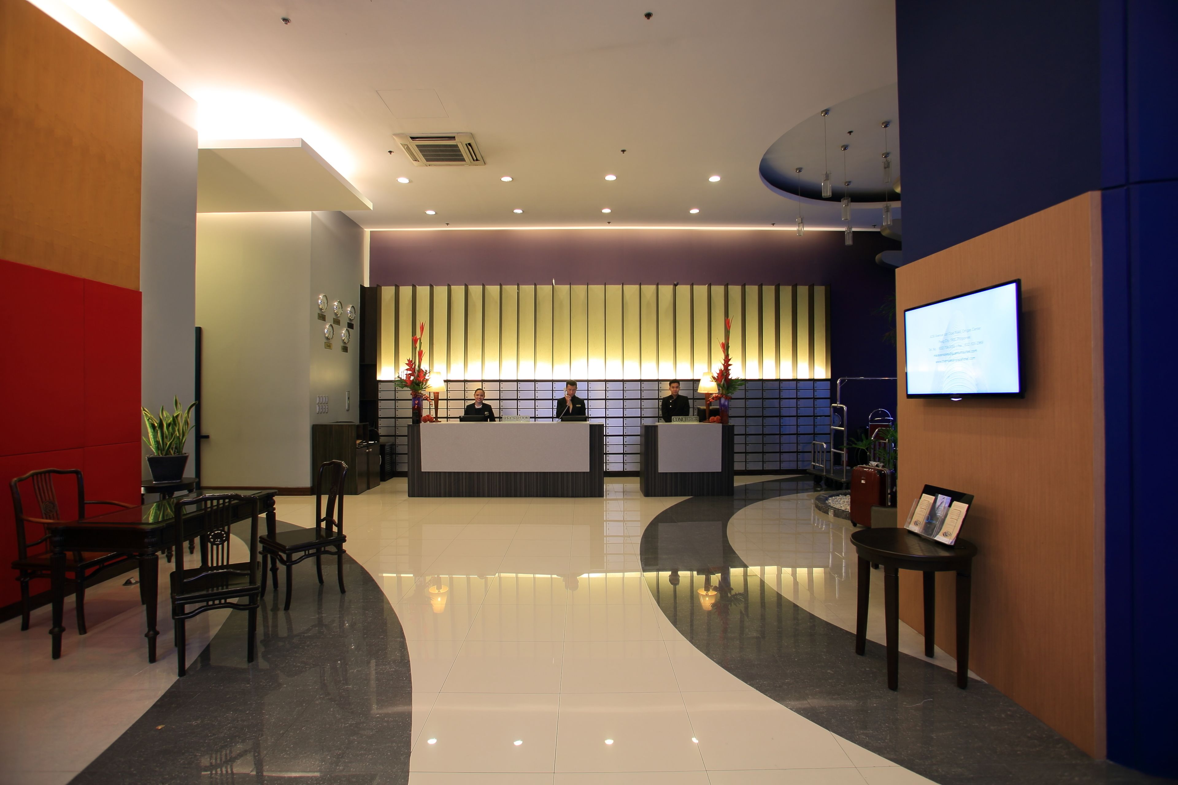 A hotel reception area with a modern design, featuring a reception desk, seating area, and a large screen displaying information.