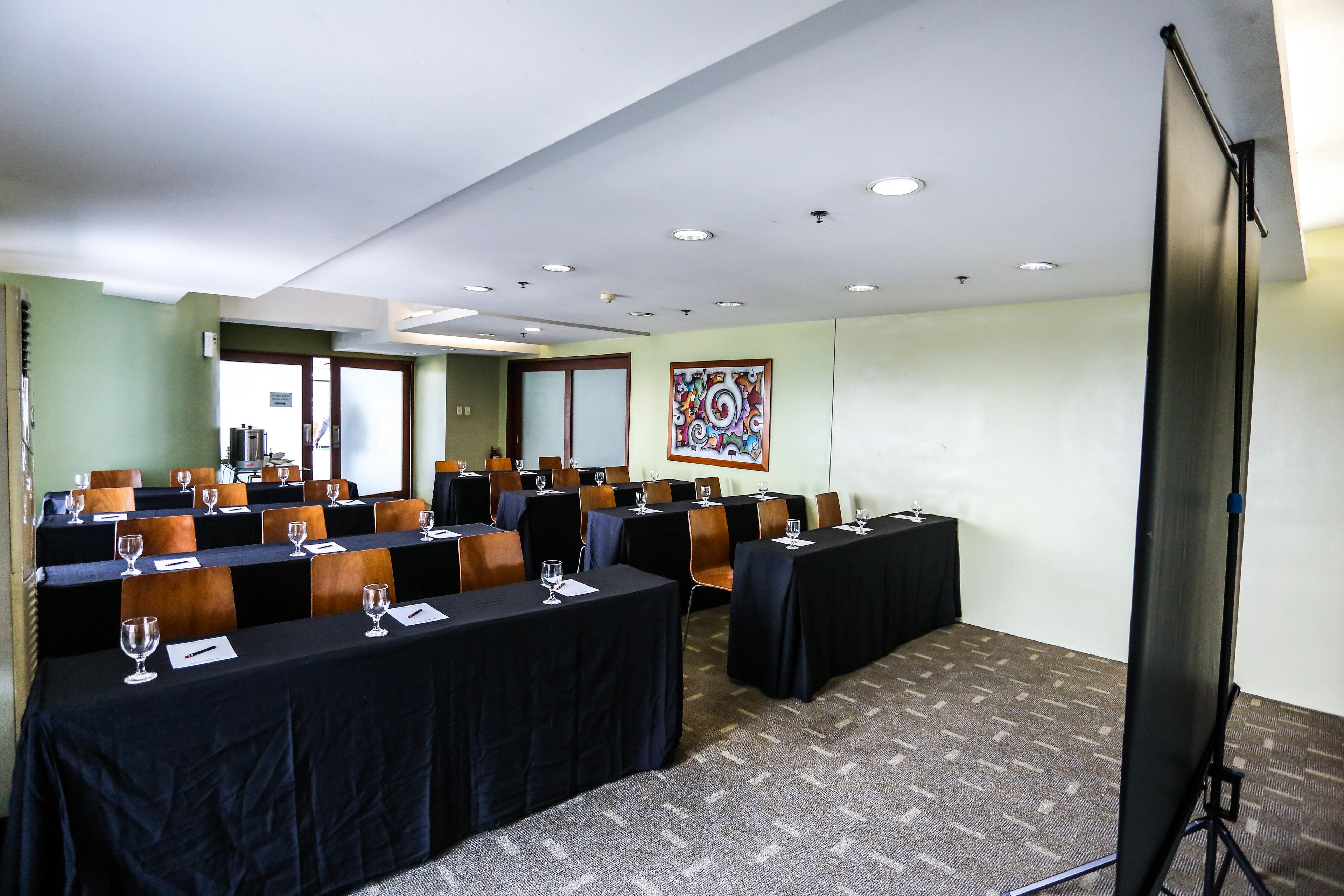 A conference room with multiple tables, chairs, and a projector screen.