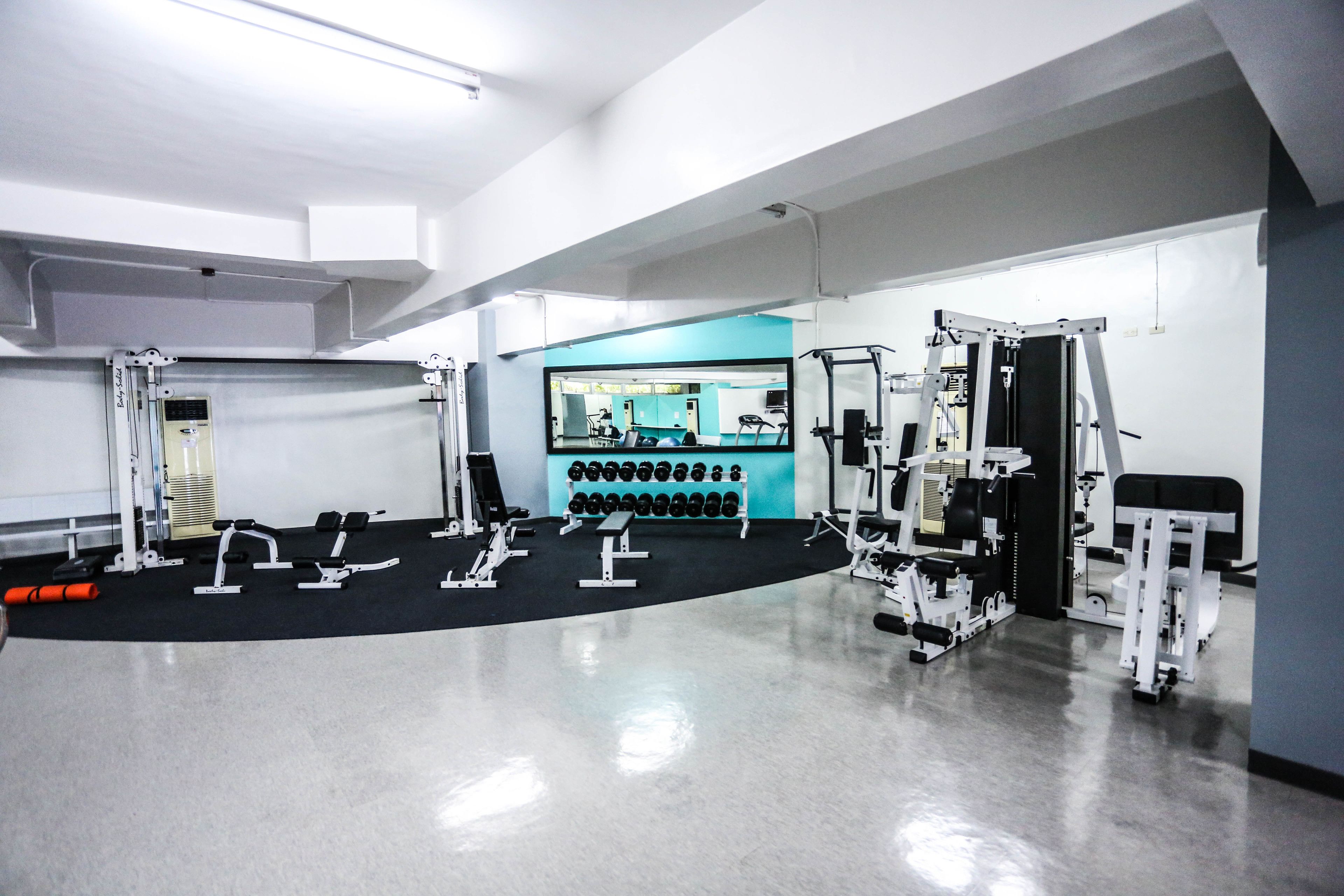 A gym with various exercise equipment, a mirrored wall, and a row of dumbbells.
